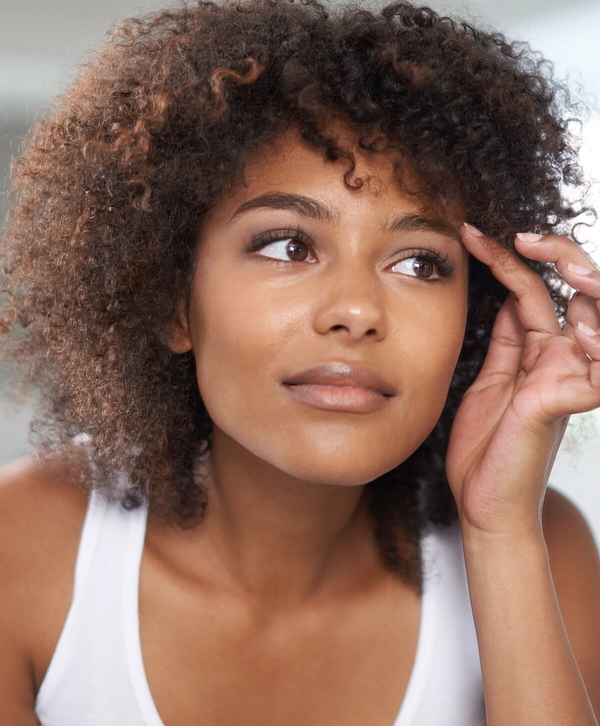 Orange County Upper Face Rejuvenation model with curly hair looking thoughtfully upward.